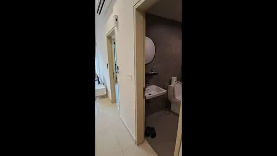 Room features: white painted walls, cream tiled flooring, round mirror, wall-mounted shelf, toilet, bidet spray, bathtub, shower, sliding door, door frame, light fixture; style: modern.