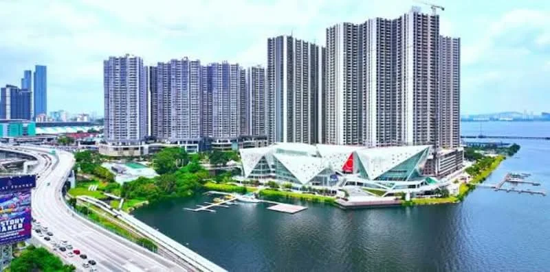 Exterior type: high-rise condominium; features: glass curtain wall, modern architectural design, waterfront view, surrounded by greenery, multiple high-rise towers, marina with boat docks, road access, urban skyline in background; style: modern.