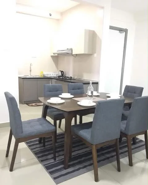 Dining features: 6-seater dining table, wooden dining table, upholstered dining chairs in grey, area rug with striped pattern, white plates on the table, glass water bottle, wall-mounted kitchen cabinets, stainless-steel range hood, built-in kitchen appliances, cream painted walls, tile flooring; style: modern. Kitchen features: grey cabinetry, stainless-steel sink, built-in stove, kitchen countertop, kitchen backsplash, kitchen utensils visible; style: modern.