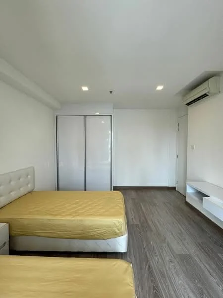 Bedroom features: two single beds with yellow bedding, white upholstered headboard, built-in wardrobe with sliding doors, white wall-mounted shelf, wooden flooring, recessed downlights, wall-mounted air conditioning unit, plain white walls; style: modern.