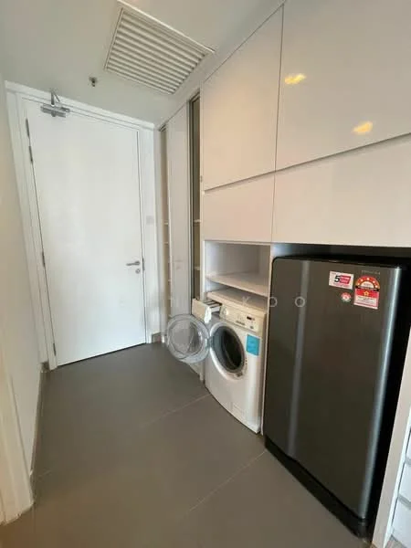 Laundry features: white cabinetry, grey tiled flooring, front-load washing machine, stainless-steel fridge, white walls, door with handle, built-in shelving, ventilation grille; style: modern.
