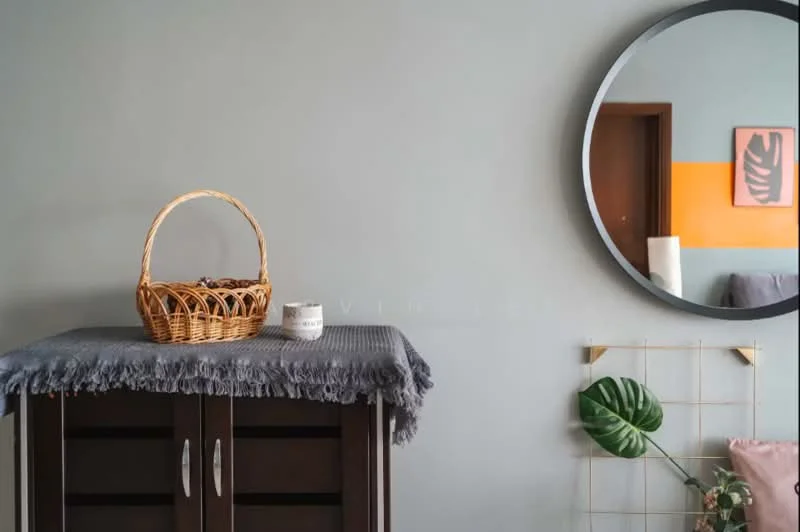 Room features: grey painted walls, wooden cabinet, woven basket, textured throw blanket, round mirror, decorative wall grid, green plant, orange accent wall, framed artwork; style: modern.