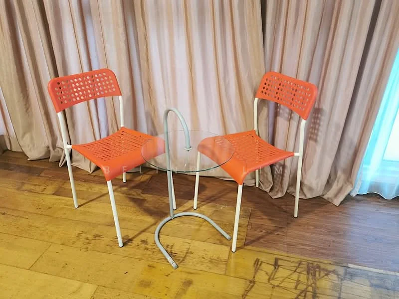 Room features: two orange chairs with perforated design, glass round table, wooden flooring, curtains in light beige, natural light from window; style: modern.