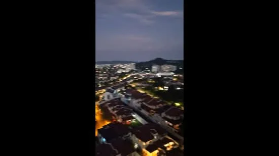 Exterior type: high-rise condominium; features: city skyline view, nighttime lighting, surrounding residential area, hills in background; style: modern.