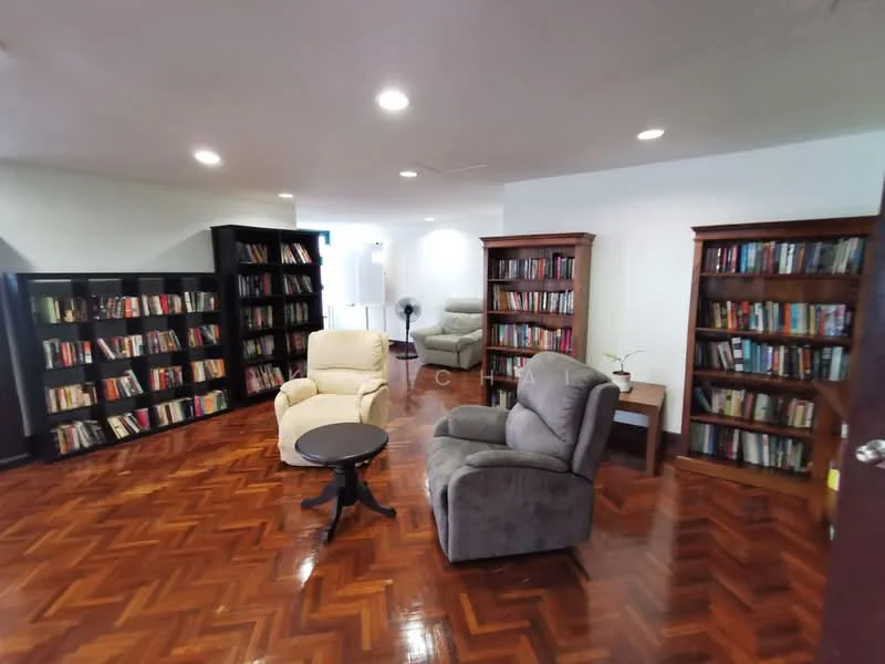 Living features: parquet wood flooring, white painted walls, recessed downlights, two bookshelves filled with books, one beige armchair, one grey armchair, round black coffee table, ceiling fan, large window with natural light; style: contemporary.