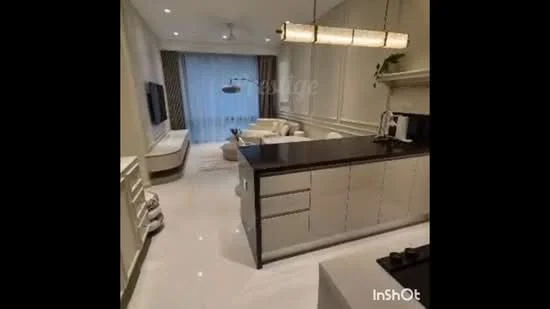 Living features: white painted walls, marble flooring, 5-blade ceiling fan with light, sofa in cream color, coffee table, TV console, wall-mounted TV, curtains with floral pattern, decorative wall paneling, pendant light fixture, kitchen island with dark countertop, built-in cabinetry, kitchen appliances including coffee machine; style: modern.