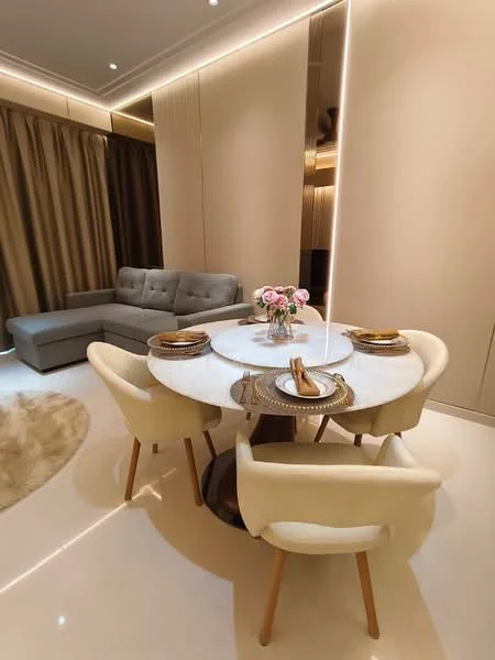 Dining features: round marble dining table, 4 upholstered dining chairs in cream, decorative table setting with plates and cutlery, floral centerpiece in vase, light-colored wall with recessed lighting, curtains in a warm tone, soft area rug, grey fabric sectional sofa in background, glossy tile flooring; style: modern.