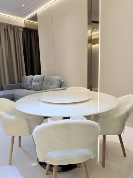 Dining features: round dining table with white marble top, 4 upholstered dining chairs with white fabric, light wood legs on chairs, decorative circular tray on table, floor-to-ceiling curtains in beige, sofa in grey fabric in background, recessed lighting in ceiling, neutral wall colour; style: modern.