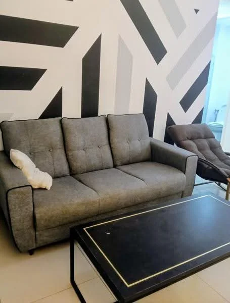 Living features: 3-seater fabric sofa in grey, accent chair in brown, black coffee table with gold trim, geometric patterned accent wall in black and white, tile flooring in light color, decorative throw pillow on sofa; style: modern.