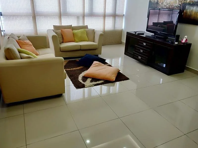 Living features: beige fabric sofa, 2-seater sofa, 3-seater sofa, decorative cushions in orange and green, area rug with geometric pattern, flat-screen TV on console, dark wood TV console, glossy tile flooring, large windows with sheer curtains, wall-mounted artwork, coffee table; style: modern.