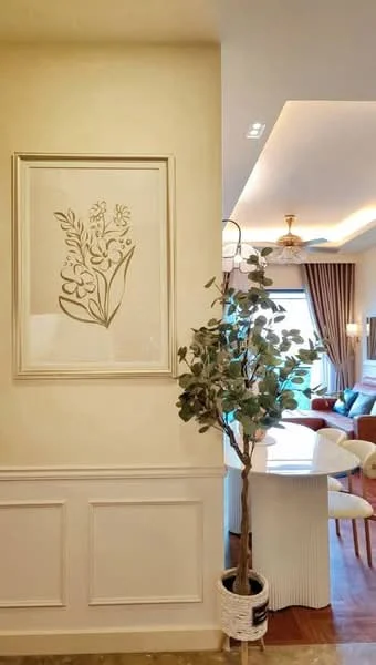 Room features: cream painted walls, crown moulding, wooden flooring, decorative wall art, indoor plant in pot, recessed downlights, curtains, dining table with chairs visible in background; style: modern.