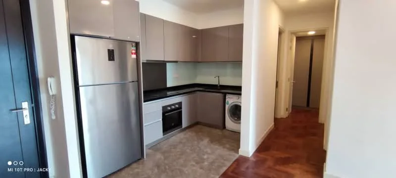 Kitchen features: grey flat-panel cabinets, black granite countertop, stainless-steel fridge, built-in oven, ceramic cooktop, single-bowl stainless-steel sink, chrome pull-down faucet, washing machine, tile backsplash, laminate flooring, recessed downlights; style: modern. Room features: doorway leading to hallway, light-colored walls, laminate flooring.