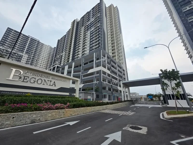 Exterior type: high-rise condominium; features: modern facade with glass and concrete, multi-storey car park, landscaped garden with flowers, guard house at entrance, wide driveway, signage with 'Residensi Begonia', surrounded by mature greenery, gated entry; style: modern.
