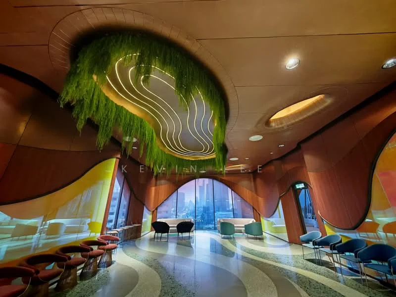 Room features: curved wooden walls, greenery feature on ceiling, modern lighting design, large windows with city view, polished stone flooring, colorful seating areas, decorative ceiling with wave pattern, ambient lighting, open layout; style: modern; view: city.