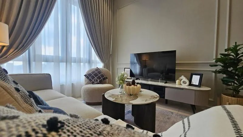 Living features: 3-seater fabric sofa in light color, accent chair, coffee table with round top, wall-mounted TV, decorative vase with flowers, textured throw blanket, large windows with sheer curtains, decorative cushions, area rug with geometric pattern, indoor plant; style: modern.
