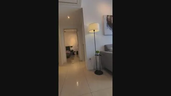 Room features: white painted walls, glossy tile flooring, recessed downlights, floor lamp, decorative artwork on wall, sofa, doorway leading to another room; style: modern.