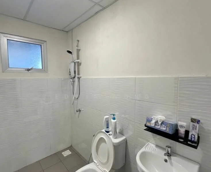 Bathroom features: white tiled walls, grey tiled flooring, toilet, sink, shower with wall-mounted showerhead, window for natural light, soap dispenser, toilet paper holder, shelf with toiletries.