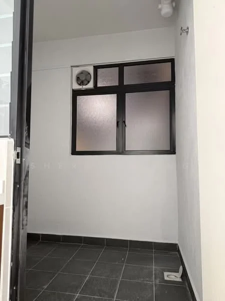 Room features: black tiled flooring, white painted walls, frosted glass window, wall-mounted fan, ceiling light fixture, corner drainage outlet.