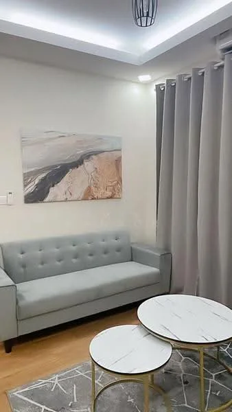 Living features: light grey fabric sofa with tufted back, two round coffee tables with marble tops and gold frames, light wood flooring, grey area rug with geometric pattern, white painted walls, recessed ceiling lights, curtains in light grey fabric, framed abstract artwork on wall; style: modern.