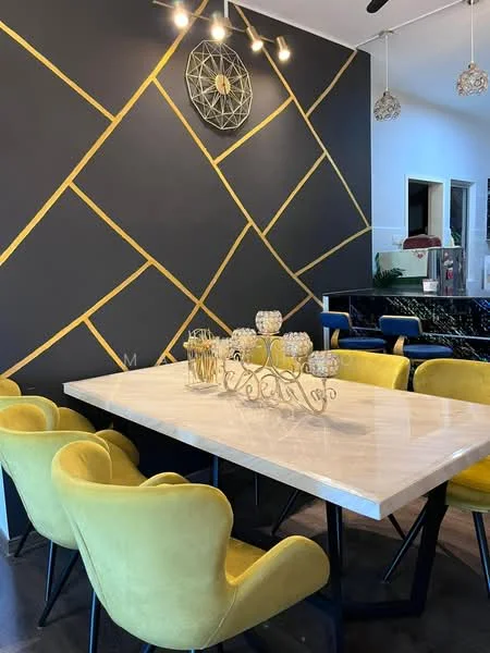 Dining features: marble dining table, yellow upholstered dining chairs, black metal legs on table, geometric accent wall with gold lines, decorative wall clock, pendant lighting fixtures, dark cabinetry in background, open kitchen view, decorative centerpiece on table; style: modern.