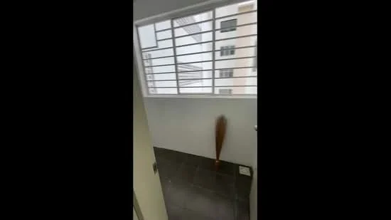 Room features: grey tiled flooring, large window with horizontal metal grilles, plain white walls, door leading to another space.