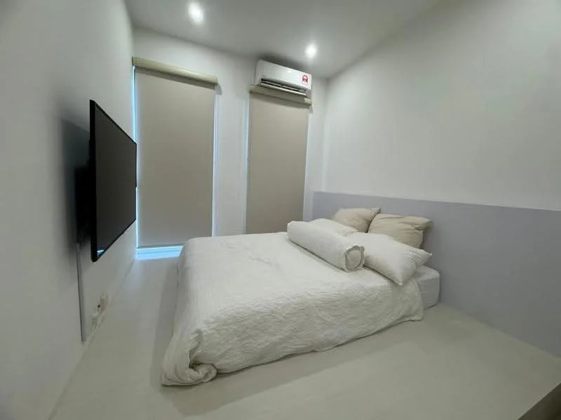 Bedroom features: queen-size bed with white bedding, two beige pillows, wall-mounted flat-screen TV, 1 wall-mounted split AC, white painted walls, light-colored flooring, roller blinds on windows, minimalist decor; style: modern.