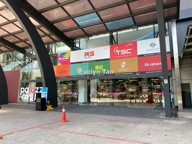 Exterior type: shopping mall; features: glass facade, canopy entrance, signage for various stores, paved walkway, parking area, traffic cones, modern architectural design; style: contemporary.