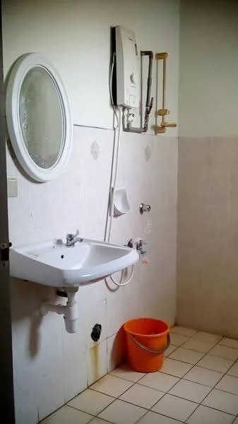 Bathroom features: white ceramic sink, chrome basin mixer faucet, round framed mirror, white tiled walls, light beige tiled flooring, water heater mounted on wall, shower head with wall-mounted holder, orange plastic bucket.
