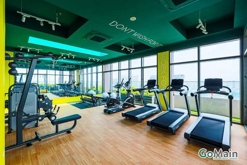 Gym features: treadmill, elliptical machine, stationary bike, weight training machine, large windows, wooden flooring, green accent walls, ceiling lights, mirrored wall, motivational wall art; style: modern; view: city.