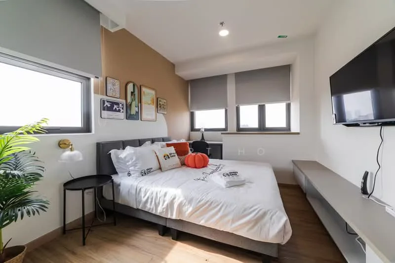 Bedroom features: queen-size bed with white bedding, upholstered headboard, decorative pillows, nightstand with lamp, wall-mounted TV, floating shelf, two windows with roller blinds, wooden flooring, potted plant, accent wall in beige, framed artwork on walls; style: modern; view: city.