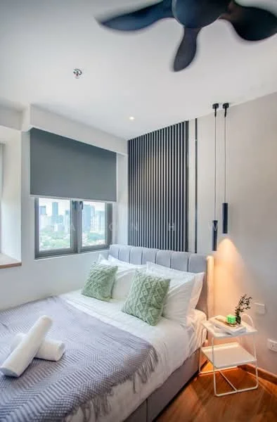 Bedroom features: queen-size bed with grey upholstered headboard, white bedding with decorative pillows, light grey throw blanket, 2 white towels, wooden flooring, floor-to-ceiling window with grey roller blinds, wall-mounted reading light, decorative plant on side table, ceiling fan with 3 blades, accent wall with vertical wooden slats; style: modern; view: city.