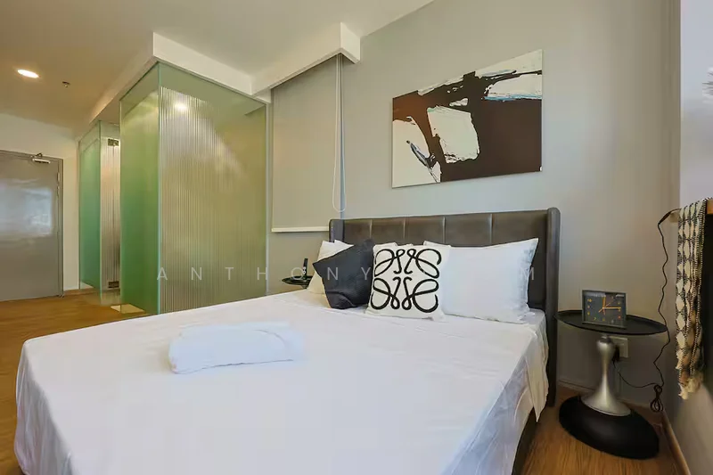 Bedroom features: queen-size bed with white bedding, upholstered headboard in grey, decorative black and white throw pillow, wooden flooring, abstract wall art, glass partition wall, nightstand with clock, white towel on bed, sheer window treatments; style: modern.