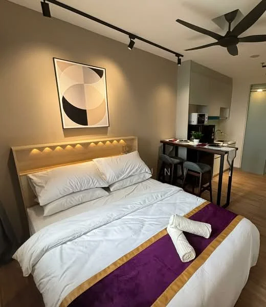 Bedroom features: queen-size bed with white bedding, wooden headboard with integrated lighting, purple and gold accent throw, 5-blade ceiling fan, wall-mounted artwork with geometric design, wooden flooring, small dining table with two chairs, kitchenette with cabinets and appliances visible; style: modern.