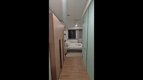 Room features: wooden flooring, white walls, ceiling fan, large window with sheer curtains, sofa bed, decorative pillows, light fixture on ceiling, built-in wardrobe, neutral color scheme; style: modern; view: city.