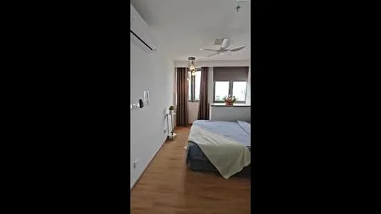 Bedroom features: wooden flooring, white painted walls, 5-blade ceiling fan with light, floor-to-ceiling window, curtains, queen-size bed with light bedding, decorative plant on nightstand, wall-mounted air conditioning unit, table lamp on nightstand; style: modern; view: city.