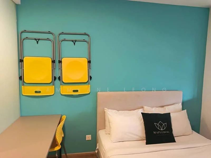 Room features: blue painted walls, light wood flooring, single bed with white bedding, decorative black pillow with logo, desk with light wood surface, yellow folding chairs mounted on wall, window with natural light, minimalist decor; style: modern.