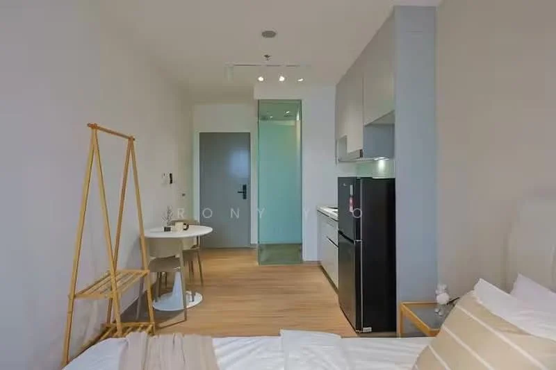 Room features: wooden flooring, white painted walls, recessed downlights, kitchenette with countertop, black fridge, small dining table for two, chair, open layout, bed with beige bedding, clothes rack, doorway to bathroom, glass panel door, light-colored cabinetry; style: modern.