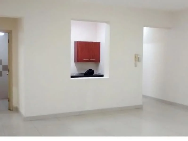 Room features: white painted walls, light grey floor tiles, window opening to kitchen area, kitchen cabinetry in wood finish, black countertop, doorway leading to another room, doorway leading to bathroom, no visible furniture or decor; style: modern.