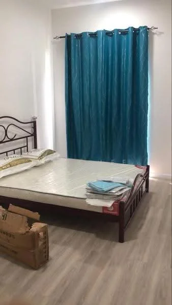 Bedroom features: queen-size bed, light wood flooring, blue curtains, white painted walls, bedding on bed, cardboard box on floor.