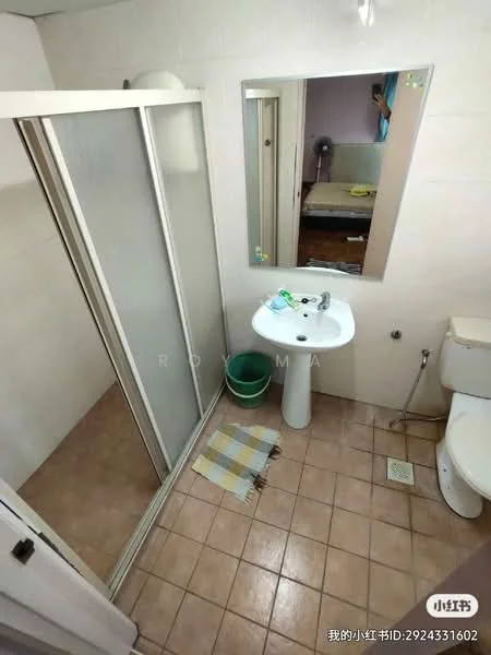 Bathroom features: shower enclosure with sliding doors, white pedestal sink, chrome basin mixer faucet, toilet, beige tiled walls, brown tiled flooring, mirror above sink, small waste bin, bath mat, towel rack.