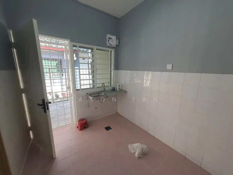 Room features: grey painted walls, white tiled walls, pink tiled flooring, single-bowl stainless-steel sink, wall-mounted faucet, window with security bars, door leading outside, floor drain, cleaning mop on floor.
