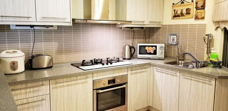 Kitchen features: light wood cabinetry, grey countertop, stainless-steel built-in oven, 4-burner gas hob, stainless-steel range hood, microwave, toaster, rice cooker, stainless-steel sink, chrome pull-down faucet, tile backsplash in beige, wall-mounted storage, decorative wall art; style: modern.