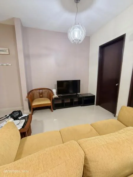 Living features: beige fabric sofa, wooden armchair, black TV console, flat-screen TV, light fixture with pendant design, cream painted walls, glossy tile flooring, dark wooden door, side table with magazines; style: modern.