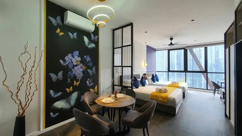 Room features: two single beds with grey bedding, decorative pillows in blue, round dining table with four chairs, wall-mounted air conditioning unit, ceiling fan, large floor-to-ceiling windows, black accent wall with floral design, light fixture with circular design, grey tiled flooring, decorative wall art with butterflies, wooden partition, natural branches in a vase; style: modern; view: city.