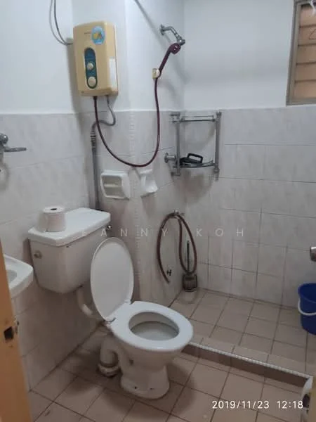 Bathroom features: white tiled walls, light beige tiled flooring, one-piece toilet, chrome basin mixer faucet, shower head with wall-mounted holder, water heater unit, toilet paper holder, shelf for toiletries, waste bin.