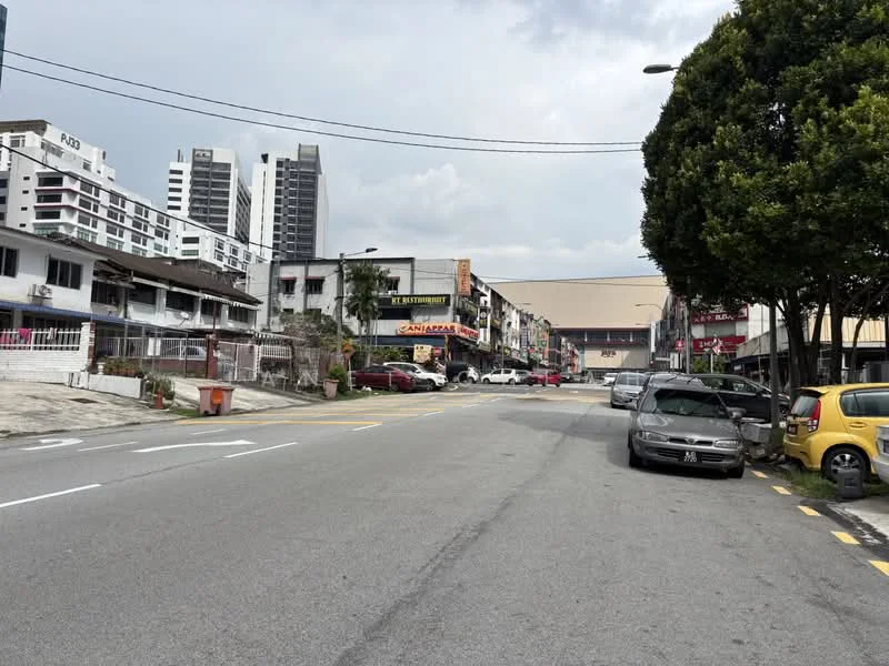 Exterior type: shophouse; features: street view, mixed-use buildings, two-storey shophouses, commercial signage, paved road, sidewalk, parking spaces, urban setting, mature trees, overcast sky; style: modern.