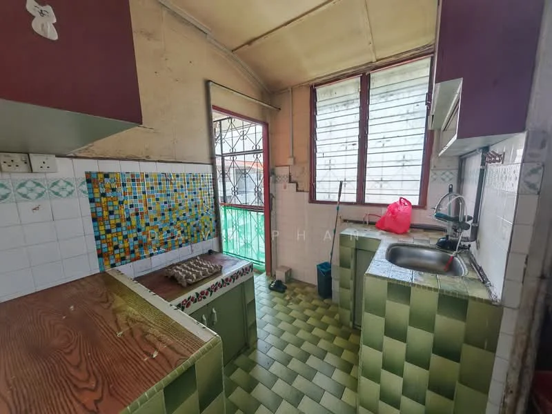 Kitchen features: green and white checkered tile flooring, white tiled walls with colorful mosaic backsplash, single-bowl stainless-steel sink, chrome pull-down faucet, wooden cabinetry in green, window with metal grilles, natural light from windows, gas stove with multiple burners, countertop space, kitchen utensils visible.