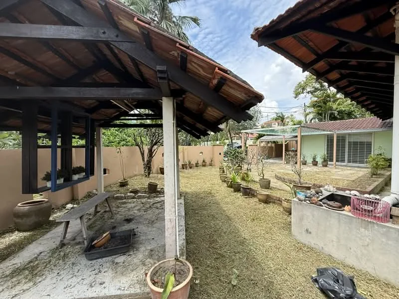 Exterior type: detached bungalow; features: thatched roof, open-air structure, concrete flooring, landscaped garden, decorative pots, fenced yard, mature trees, grassy area, outdoor seating area, garden pathway; style: tropical-modern.