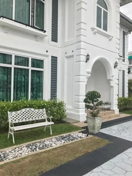 Exterior type: detached bungalow; features: white painted facade, arched entrance, green tinted windows, decorative stone pathway, manicured lawn, landscaped garden with shrubs, outdoor bench, potted plant, grey siding, stone cladding at base; style: modern.