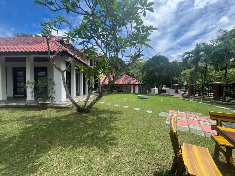 Exterior type: detached bungalow; features: red tiled roof, white painted facade, manicured lawn, mature trees, stone-paved walkway, outdoor seating area with wooden chairs, landscaped garden, fenced perimeter; style: tropical-modern.